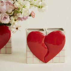 two heart shaped vases sitting next to each other with flowers in the back ground