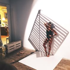 a woman standing in front of a white wall with her shadow on the wall behind her