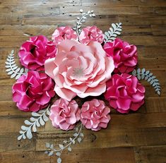 pink paper flowers are arranged on a wooden floor with silver leaves and branches around them