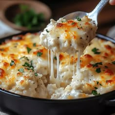 a spoon full of macaroni and cheese being lifted from a skillet with a fork