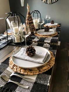 a dining room table set for christmas with plates, silverware and pine cone decorations