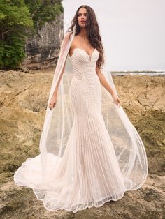 a woman in a wedding dress standing on the beach with her veil over her head