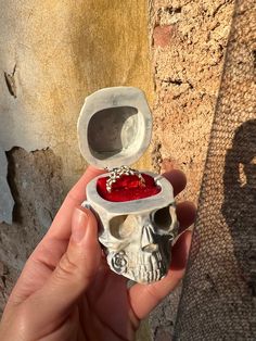 a hand holding a skull ring with a red stone in it's center and inside