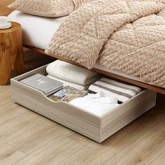 an open drawer underneath a bed in a room with wood floors and white sheets on it