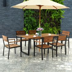 an outdoor table with chairs and umbrella in front of a wall covered with greenery