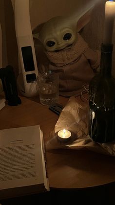 an alien doll sitting on top of a table next to a book and some candles