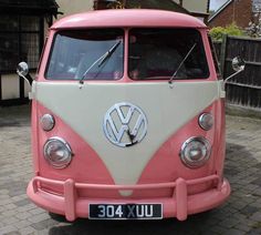 a pink and white vw bus parked in front of a brick building on the street