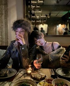 two women sitting at a table with food and drinks in front of them, both looking at their cell phones