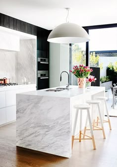 a kitchen with marble counter tops and stools in front of the island, surrounded by white cabinets