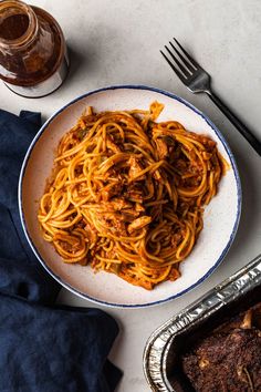 a white plate topped with spaghetti and meat next to a fork, knife and spoon