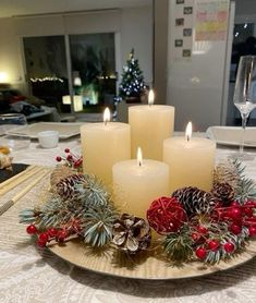 three lit candles sitting on top of a plate covered in pine cones and red berries