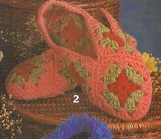 two crocheted slippers sitting on top of a basket next to some flowers