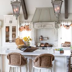 a kitchen with two stools in front of an island and some hanging lights above it