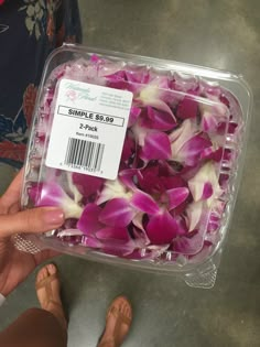 a plastic container filled with pink and white flowers next to someone's bare feet