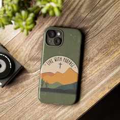 a phone case sitting on top of a wooden table next to a camera and plant