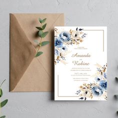 an elegant wedding card with blue flowers and greenery on the front, next to a brown envelope