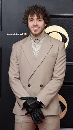 a man in a tan suit and black gloves on the red carpet at an awards event