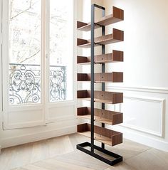 a tall book shelf sitting in the corner of a living room next to a window