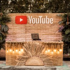 a sign that says youtube is displayed in front of some plants and trees with lights around it