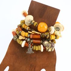 Beaded Stretch Bracelets. Indulge in the unique charm of these handmade Stackable Bracelets, designed to add a touch of boho chic to your style. Crafted with an array of materials including Horn, Czech glass, orange resin, bone, brass, and Thailand rustic glass.  These bracelets are versatile enough for solo wear or for stacking with others. The earthy color palette of light orange, rustic yellow, brass and off white will complement various outfits. With a comfortable fit for small wrists ranging from 6" to 6.50", these bracelets are strung with professional stretch cord.  Delivered in a gift box or bag, they make for a perfect present or a stylish treat for yourself. Available per bracelet or mix and match. Complete set is available - see photos for pricing. 1.    Brass Buddha charm, Czec Bohemian Gold Stretch Bracelet For Festivals, Bohemian Multi-strand Bracelets With Large Beads, Handmade Hippie Gold Beaded Bracelets, Handmade Multi-strand Beach Bracelets, Handmade Gold Bohemian Wrap Bracelet, Bohemian Orange Beaded Bangle Bracelets, Bohemian Orange Beaded Bangle Bracelet, Orange Bohemian Beaded Bangle Bracelet, Bohemian Orange Bangle Jewelry