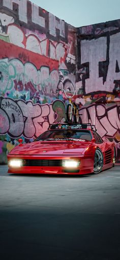 a red sports car parked in front of a wall with graffiti on it's walls