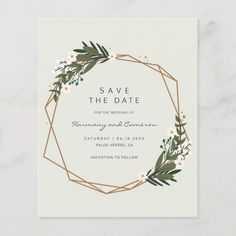 save the date card with greenery and white flowers in a gold frame on a marble background