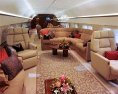 the inside of an airplane with couches, tables and flowers on the carpeted floor