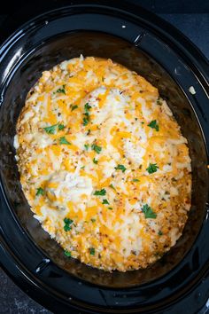 a crock pot filled with cheese and parsley on top of a black table