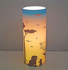 a lamp that has animals on it and birds flying in the sky over trees at sunset