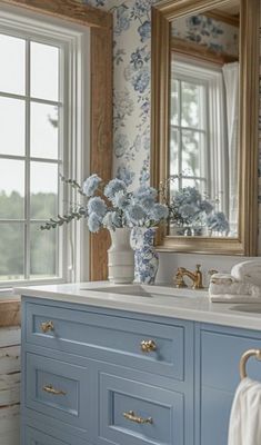 a blue and white bathroom with flowers in the vase on the sink counter, and large mirror