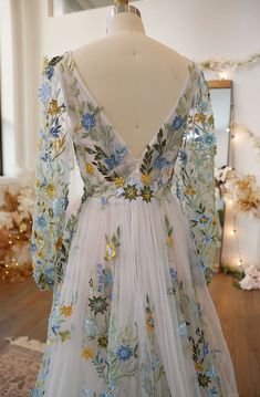 a white dress with blue and yellow flowers is on display in front of a mirror