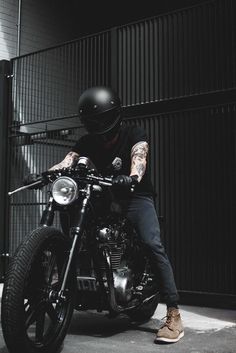 a man sitting on top of a motorcycle wearing a helmet and black pants with tattoos