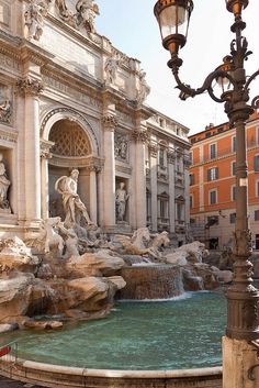 a fountain in front of a building with statues on the sides and a street light next to it