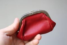 a hand holding a red purse with a metal clasp on the front and bottom side