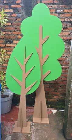 two cardboard trees sitting next to each other on top of a cement slab in front of a brick wall