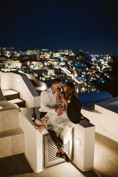 a man and woman sitting on top of a building next to each other at night