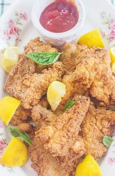 fried chicken with lemons and ketchup on a floral plate next to a small bowl of sauce