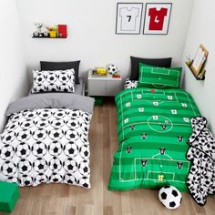 two beds in a room with soccer themed sheets and pillows on the floor, one has a soccer ball