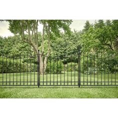 an iron fence in the middle of a grassy area with trees and bushes behind it