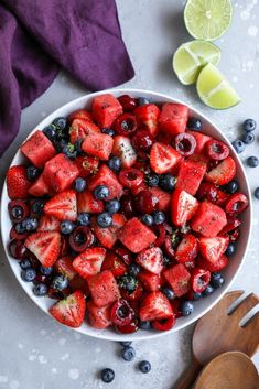 a bowl filled with berries and blueberries next to lime wedges on a table