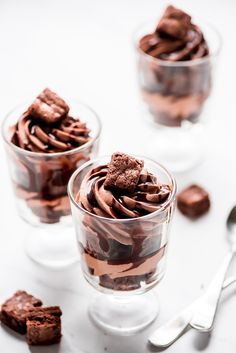 three glasses filled with chocolate desserts on top of a white table next to silverware