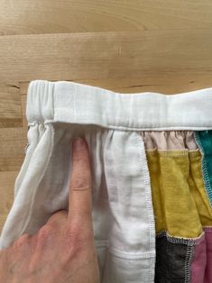 a hand is pointing at the bottom of a pair of white pants with multicolored fabric