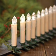 a row of lit candles sitting on top of a wooden table next to evergreen branches