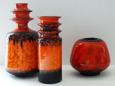 three orange and black vases sitting next to each other on a white counter top