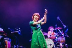 a woman in a green dress holding up a cell phone while standing next to a band on stage