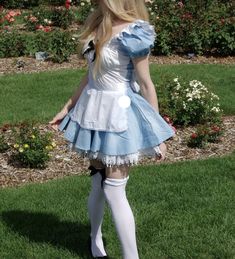 a woman in a blue dress and white stockings is standing on the grass with her back to the camera