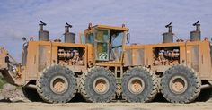 a large yellow tractor parked on top of a dirt field next to a pile of rocks