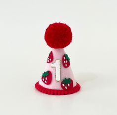 a pink and red birthday hat with strawberries on the top that says number one