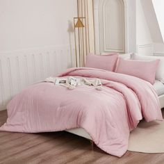 a bed with pink sheets and pillows in a white room next to a window,