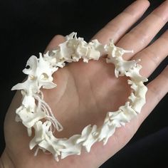 a hand is holding a white bracelet made out of plastic flowers and leaves on it